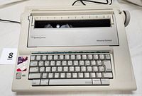 Front angle shot of off-white Smith Corona NA1HH electric typewriter showing keyboard, ribbon mechanism, and paper feed roller with ruler.