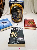Photo showing all three books from the Hunger Games trilogy (Hunger Games paperback, Catching Fire hardcover, Mockingjay hardcover) alongside the Lord of the Rings Gollum action figure in original packaging.