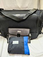 Travel bags including black Embark garment bag, grey/black Chaps organizer, and folded Izod black/blue packable jacket