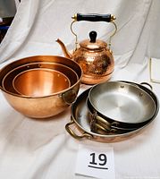 Photo showing hammered copper teapot with black handle and knob, copper nesting mixing bowls, and copper-bottom Ballarini pans with brass handles.