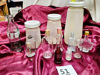 Photo showing all nine vintage glass bottles arranged on a red satin cloth with a number 51 card, showing various shapes including tall bottles and smaller cologne and ink bottles.