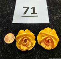 Pair of large butterscotch Bakelite rose carved pendants shown on black background with a penny for size scale.