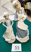Photo of two porcelain figurines: a taller farm girl holding a lamb and a smaller farm girl with hands on hips
