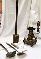 Full lot showing vintage electric light with hurricane globe, wooden-handled ladle, spatula, Bull Dog can opener, and tall wooden cylindrical mallet/pestle against white curtain backdrop.