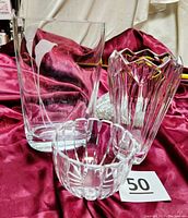 Three glassware pieces shown on burgundy satin fabric: Orrefors crystal bowl, Masaka Calla Lily vase, Lenox crystal vase with marbles.