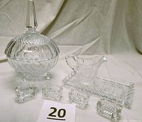Front perspective showing large lidded candy bowl on three feet, rectangular serving tray, creamer, and four small salt cellars arranged in front.