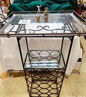 Free-standing heavy metal wine rack with 15 circular bottle slots stacked vertically, holding 2 rectangular glass shelves, top shelf and middle shelf visible. Included are 2 pewter wine stoppers on top glass shelf with golf shapes. Floor background.