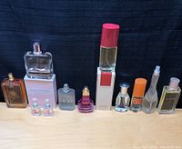 Full view of 11 perfume bottles of various sizes and brandings placed side by side on a wooden surface against a dark background.