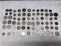Overview of 53 foreign coins arranged on a white towel showing varied sizes, shapes, and materials.