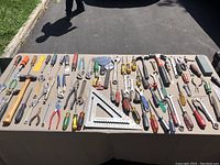 Wide shot of the tool lot showing many hand tools arranged on table.