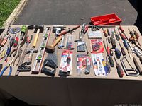 Overview of tools laid on table including level, saw, hammer, multiple pliers, screwdrivers, and tool accessories