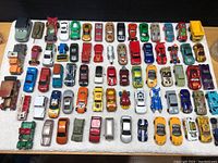 Top-down view showing multiple rows of toy cars and vehicles organized on a white surface.