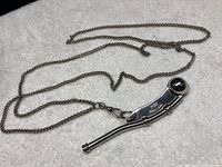 Silver boatswain pipe whistle with attached metal chain placed on white cloth background.