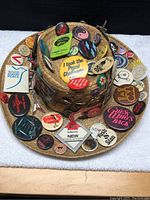 Top angled view of the straw hat covered with various vintage button pins and badges.