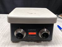 Corning PC-351 hot plate stirrer showing front panel with two knob controls and orange indicator light on, top surface visible