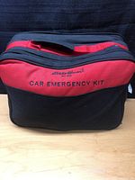 Full view of the Eddie Bauer branded black and red car emergency kit soft carrying case on a wooden surface.