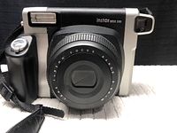 Front view of Fujifilm Instax Wide 300 camera with lens retracted and visible grip on side.