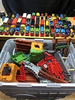 Plastic container filled with numerous red, green, brown, and gray track pieces, bridges, and tunnels for the Thomas train set.