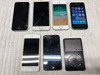 Top view of all 7 devices showing screen damage especially cracked screens on iPhones and iPods.