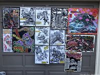 Overview of 13 assorted art prints and posters pinned on a board or wall in 2 rows. Varied themes and styles, some colorful, some black and white.