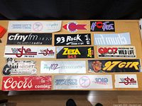 Overview photo showing all vintage radio and car stereo stickers arranged on a table including CFNY FM, WSHE FM, Zeta 94.9, 93 Rock, Pioneer Car Stereo, H105, 97 GTR, drink driving warning, Coors, and Scooby-Doo.