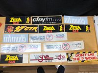 Photo of the full lot of vintage radio car stickers arranged on a table, showing various brands and slogans.