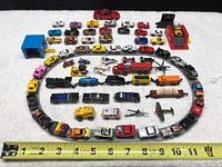 Wide shot showing all miniature vehicles displayed on a white towel with a yellow measuring tape for scale.