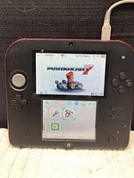 Nintendo 3DS XL handheld console powered on showing Mario Kart 7 loading screen.