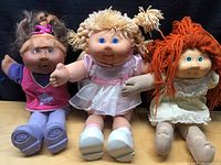 Group image of the three Cabbage Patch Kids dolls sitting side by side showing their full outfits and faces.