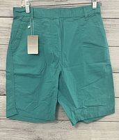 Front view of teal long shorts with both front pockets visible, hanging on a clip hanger.