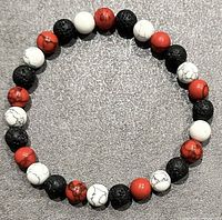 Top-down view of a beaded bracelet with black, white, and red beads arranged in a repeating pattern, laid flat on a surface.