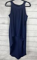 Front view of the sleeveless navy long back top hanging on a hanger against a wooden background to show style and length.