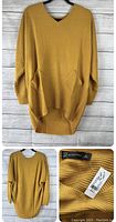 Front view of mustard yellow ribbed knit sweater on a black hanger against a wooden background.