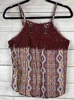 Tank top hanging on black hanger against white wood textured background showing front view with burgundy lace yoke and multicolor geometric pattern below.
