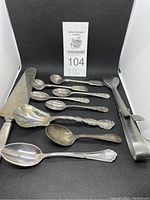 View of all 10 pieces of antique silverware showing variety of sizes and designs including spoons, knife and tongs.