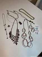 Full view of 7 necklaces, including one with matching earrings on white table
