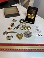 Top view of 12 assorted vintage brooches and pins arranged on a white surface with a ruler beneath them for size reference.