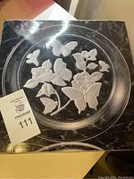 Clear glass platter with embossed butterfly and flower design, showing front view on a dark background surface.