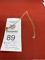 Photo showing the gold chain with the heart-shaped pendant and auction tag with lot number and description.