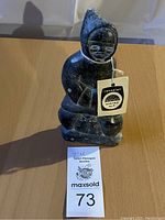 Front view of one vintage Inuit carving figure wearing hood, with tags and auction number visible