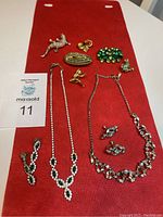 Photo showing all jewelry pieces in the lot including necklaces, earrings, and six pins arranged on a red cloth.