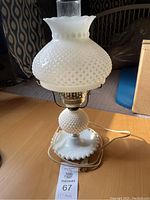 Full view of 17-inch tall milk glass lamp on wooden surface showing hobnail pattern and scalloped edge base.