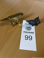 Photo of the small brass anvil and cast iron dog figurine side by side on a white surface with auction tag.