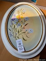 Oval floral painting in oval frame, showing blue, purple, yellow, and pink flowers with green leaves