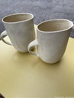 Two beige speckled pottery milk jugs with handles photographed from above showing the front and side.