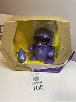 Boxed purple Meow Chi electronic robot kitten with a ripped cardboard box and yellow interior; item displayed inside box with fish accessory beside.