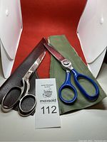 Two pairs of sewing scissors placed on fabric rectangles with sheaths, well lit and shown from above.