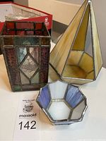 Photo showing the three stained glass candleholders together: rectangular with red and clear geometric design, pyramidal cream-colored holder, and hexagonal blue and white holder.