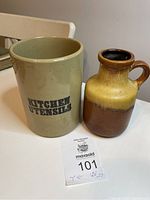 Photo showing beige English utensil holder with 'KITCHEN UTENSILS' text and brown West German jug with handle placed side by side on a white table.