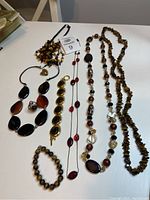 Full lot laid out on white surface showing two rings, two bracelets, and five necklaces all in brown tones with one bracelet of large round beads that appear to be tiger's eye.